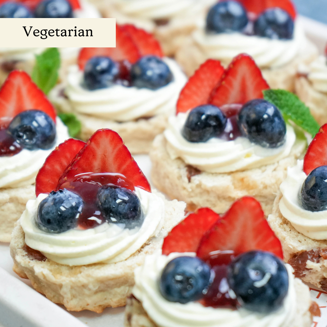 Close-up of sultana scones topped with whipped cream, strawberry jam, and fresh British summer berries