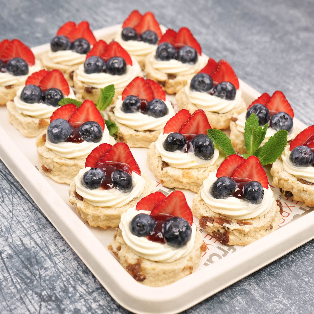 Close-up of sultana scones topped with whipped cream, strawberry jam, and fresh British summer berries