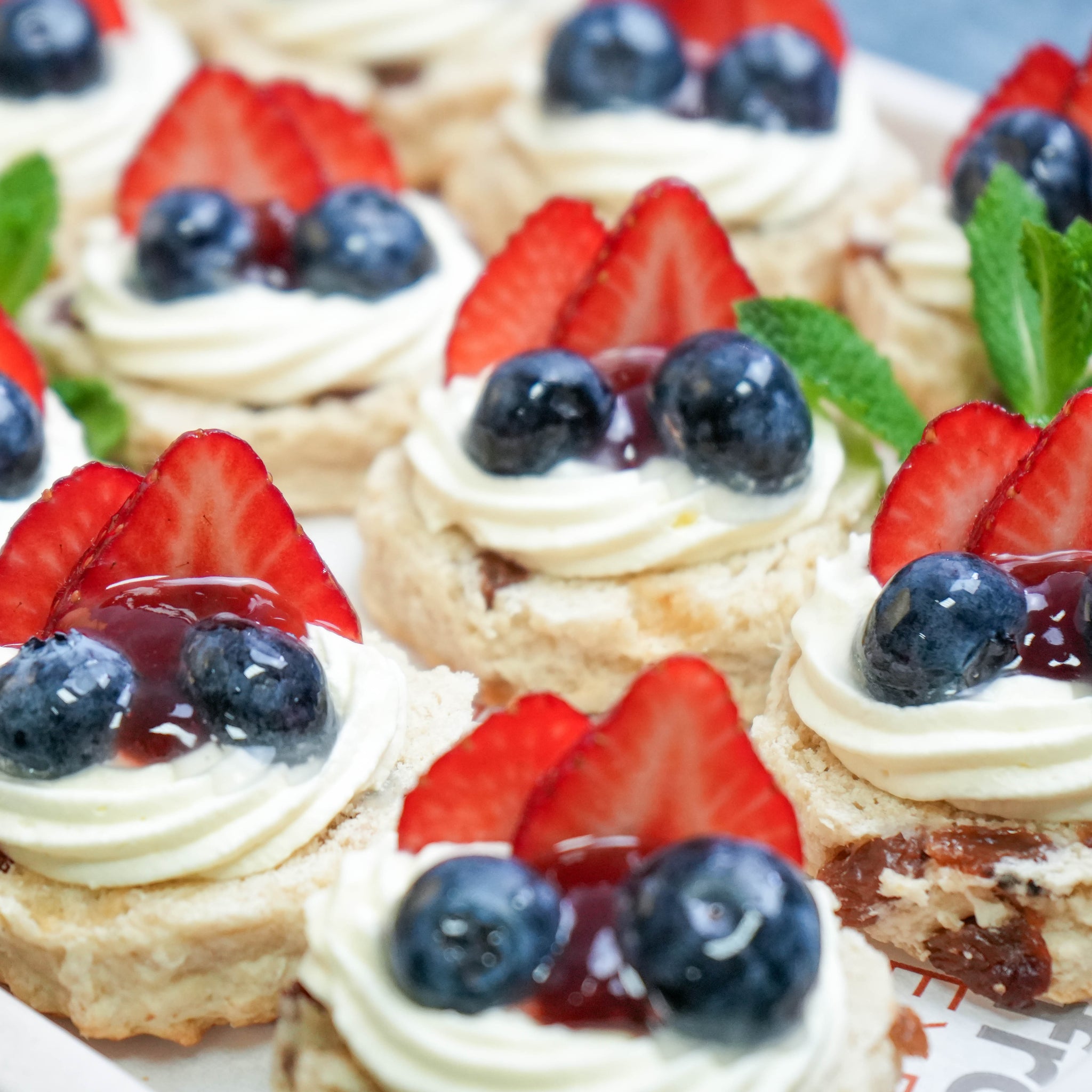 Close-up of sultana scones topped with whipped cream, strawberry jam, and fresh British summer berries