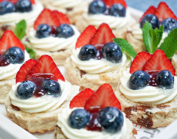 Close-up of sultana scones topped with whipped cream, strawberry jam, and fresh British summer berries